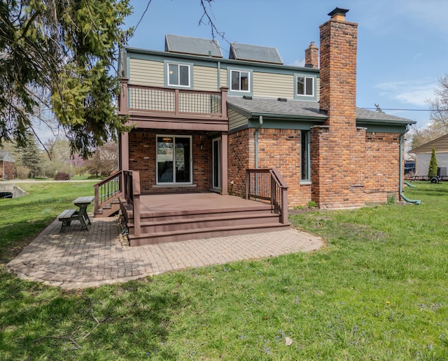 rear view of property with a chimney, a lawn, a patio area, brick siding, and a balcony