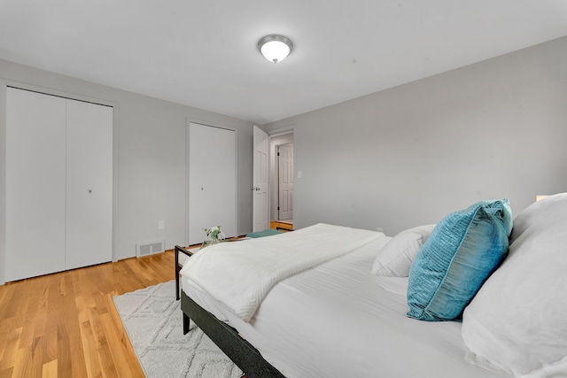bedroom with visible vents, light wood-style flooring, and two closets
