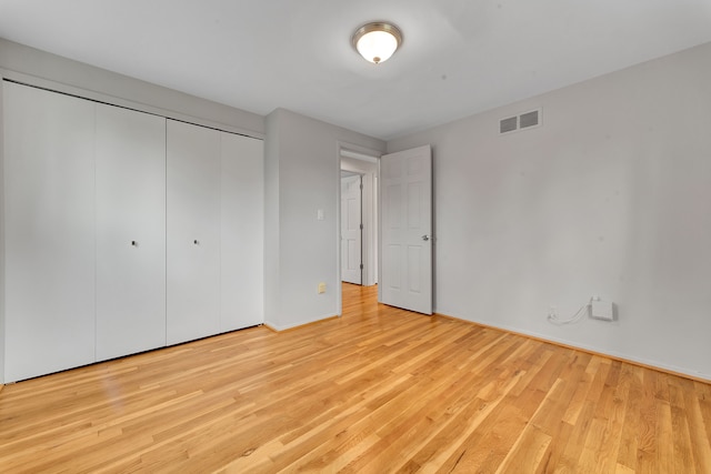 unfurnished bedroom featuring baseboards, visible vents, wood finished floors, and a closet
