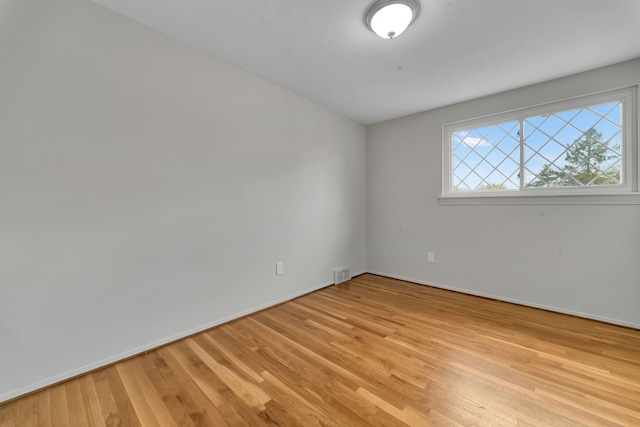 empty room with visible vents, light wood finished floors, and baseboards
