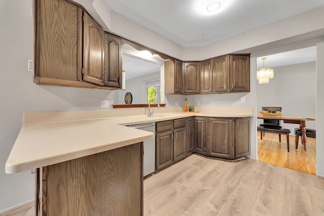kitchen featuring stainless steel dishwasher, light wood-type flooring, light countertops, a chandelier, and a sink