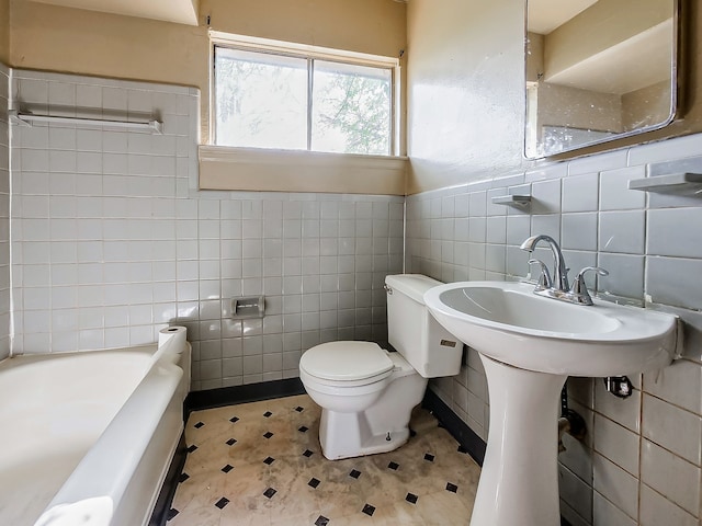 bathroom featuring tile walls, toilet, a tub to relax in, tile patterned floors, and wainscoting