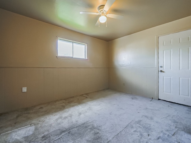 empty room featuring wainscoting, carpet flooring, and ceiling fan