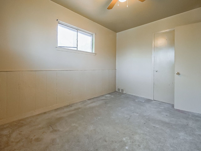 carpeted empty room featuring ceiling fan and a wainscoted wall
