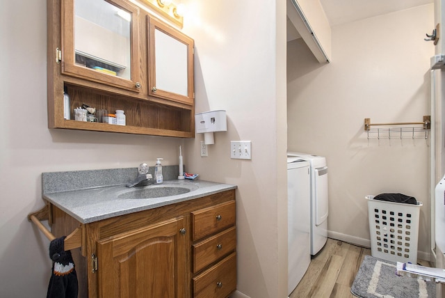 washroom featuring baseboards, washer and dryer, a sink, laundry area, and light wood-style floors