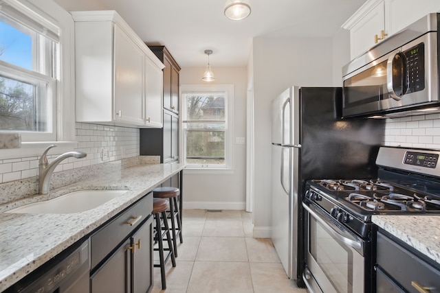kitchen with a sink, decorative backsplash, light tile patterned flooring, baseboards, and appliances with stainless steel finishes