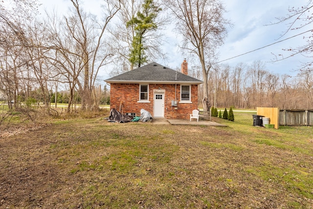 back of house with roof with shingles, a chimney, fence, brick siding, and a yard