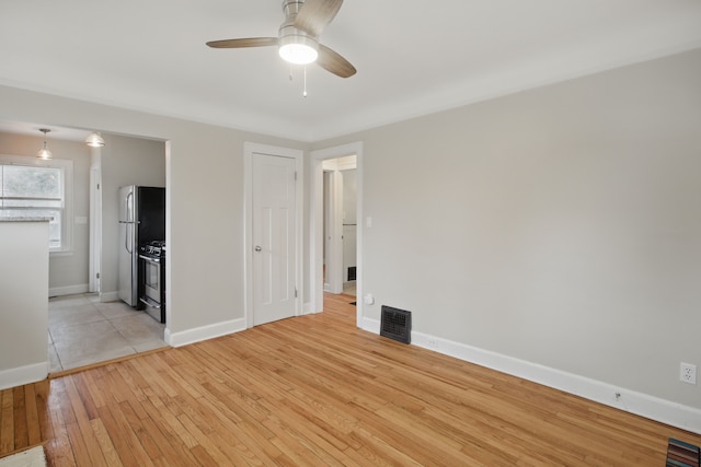 spare room with baseboards, light wood-style flooring, visible vents, and ceiling fan