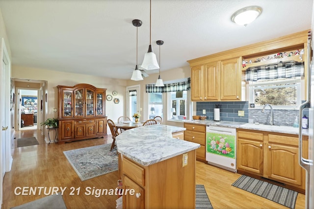 kitchen featuring tasteful backsplash, light wood-type flooring, a kitchen island, white dishwasher, and a sink