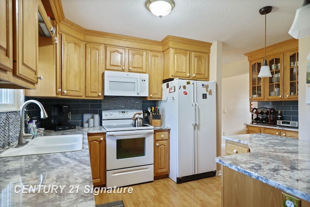 kitchen with light wood-style flooring, glass insert cabinets, a sink, white appliances, and decorative backsplash