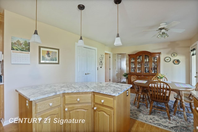 kitchen with light stone countertops, decorative light fixtures, a ceiling fan, and wood finished floors