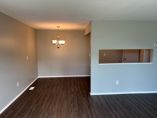 empty room with a chandelier, wood finished floors, and baseboards