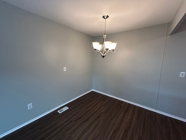 empty room with a notable chandelier, visible vents, baseboards, and dark wood finished floors