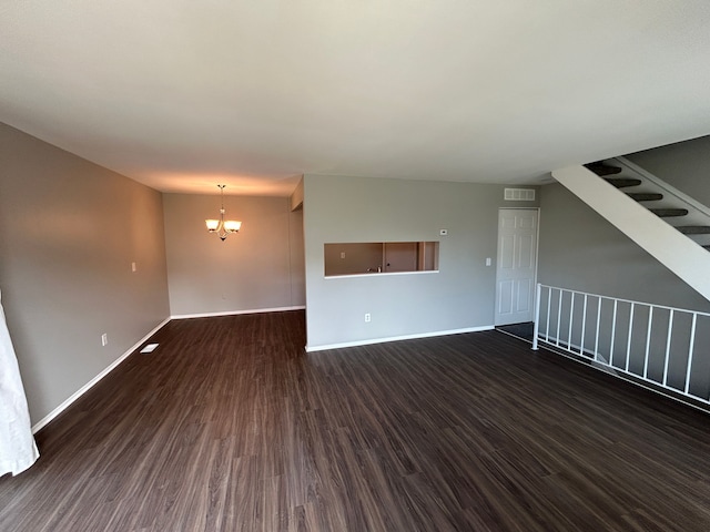 unfurnished living room with a chandelier, dark wood-style flooring, baseboards, and visible vents