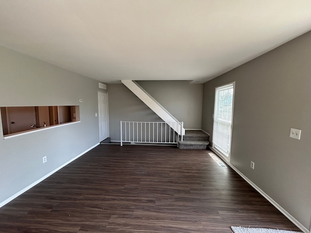 unfurnished living room with dark wood-style flooring, baseboards, and stairway