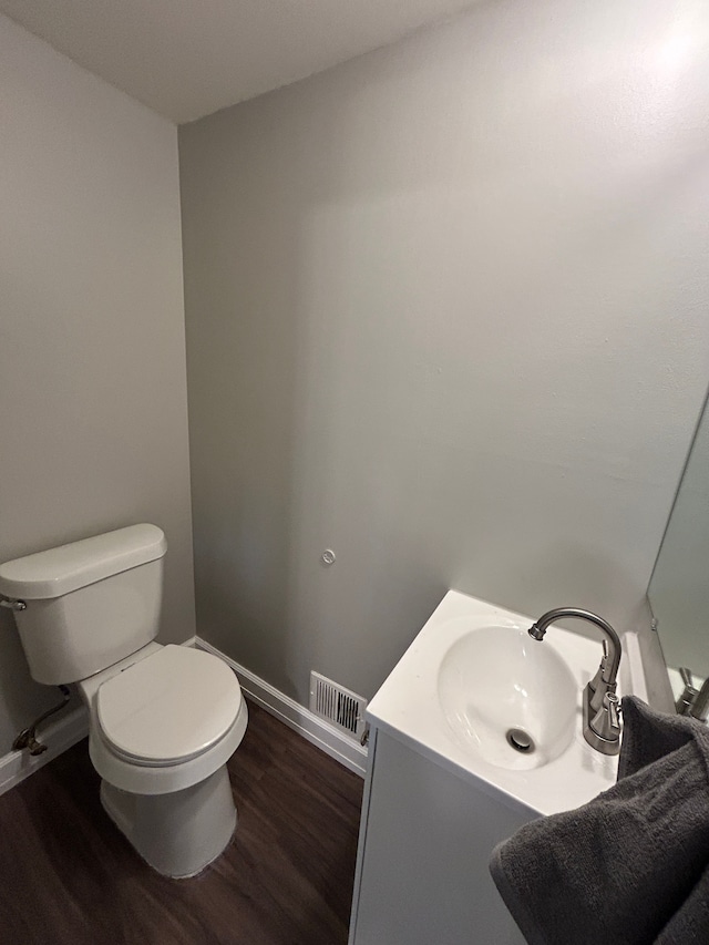 half bathroom with visible vents, baseboards, toilet, vanity, and wood finished floors