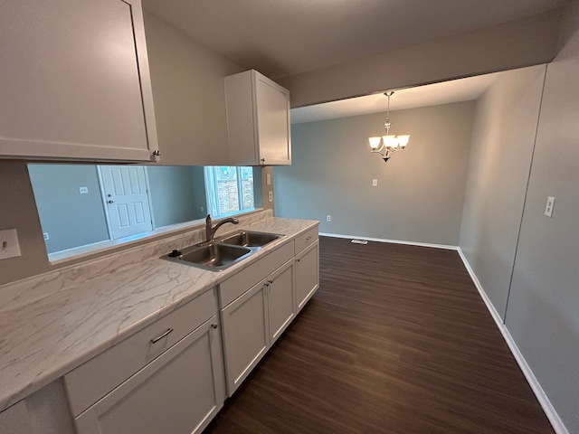 kitchen featuring baseboards, white cabinets, a notable chandelier, a sink, and dark wood finished floors