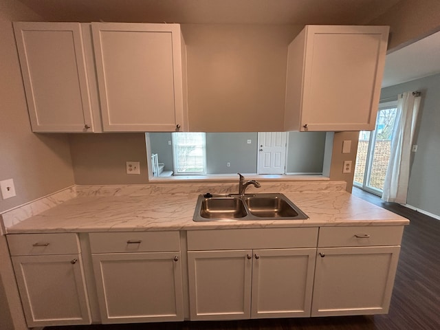 kitchen with a sink, white cabinets, light stone counters, and dark wood-style floors