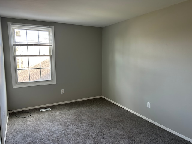 empty room with visible vents, dark colored carpet, and baseboards