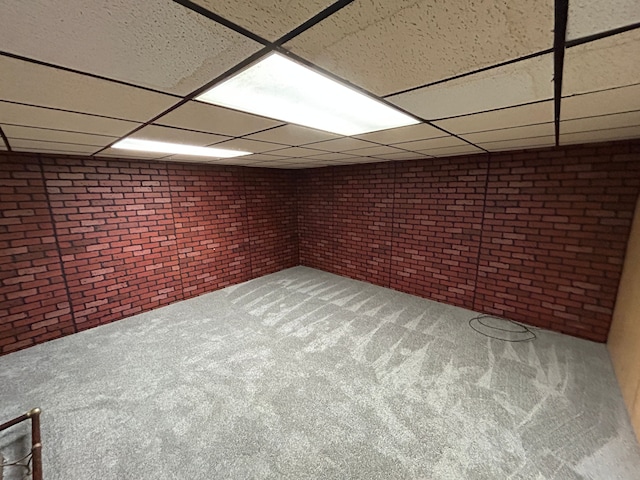 finished below grade area with a drop ceiling, carpet flooring, and brick wall