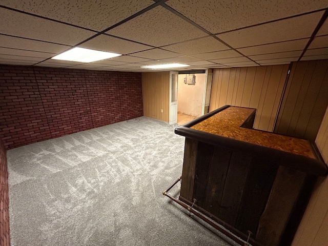 finished basement featuring brick wall, a bar, a paneled ceiling, carpet, and wooden walls