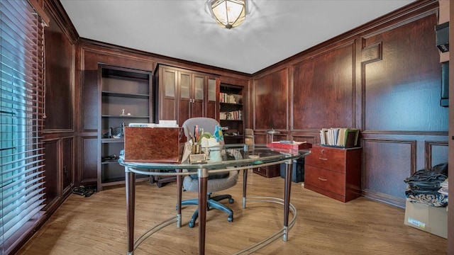 office area with a decorative wall, light wood-style floors, wooden walls, built in shelves, and ornamental molding