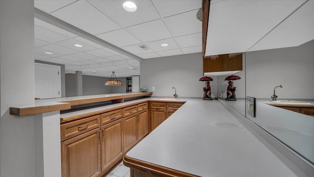kitchen with a sink, brown cabinetry, light countertops, a peninsula, and recessed lighting