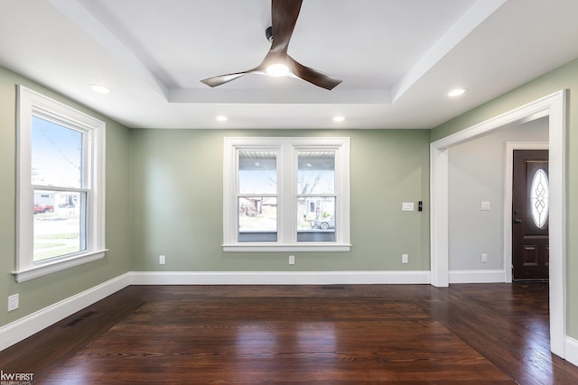 spare room featuring a raised ceiling, dark wood-style flooring, a ceiling fan, and visible vents