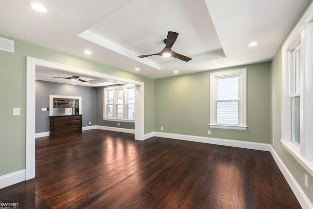 unfurnished living room featuring baseboards, a tray ceiling, a ceiling fan, and dark wood finished floors