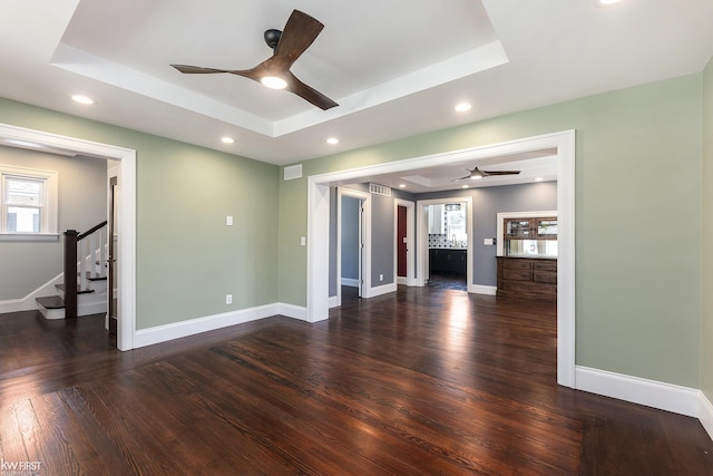 unfurnished living room featuring stairway, a tray ceiling, and a ceiling fan