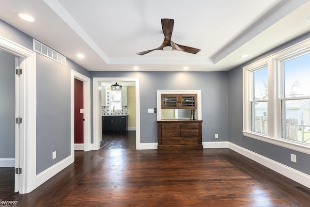 interior space with a raised ceiling, ceiling fan, visible vents, and dark wood-style flooring