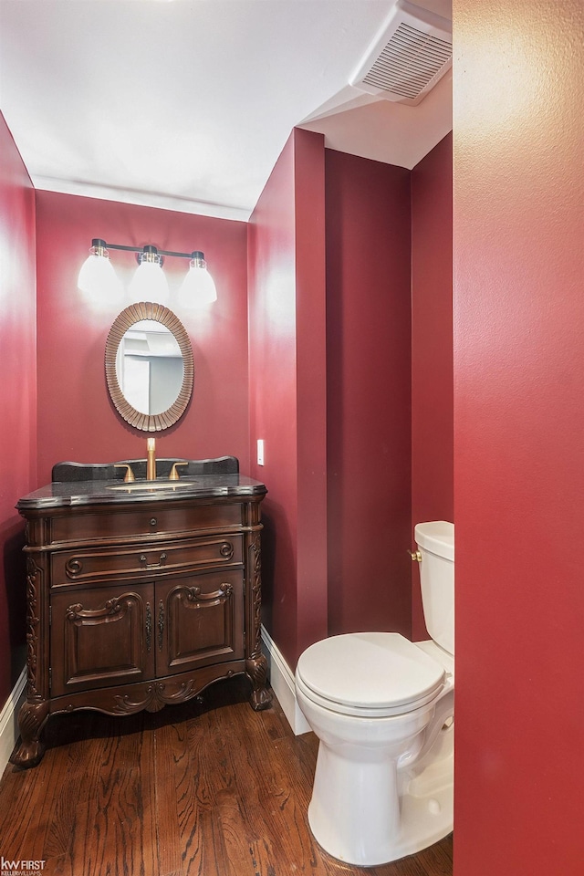 half bath with vanity, baseboards, toilet, visible vents, and wood finished floors