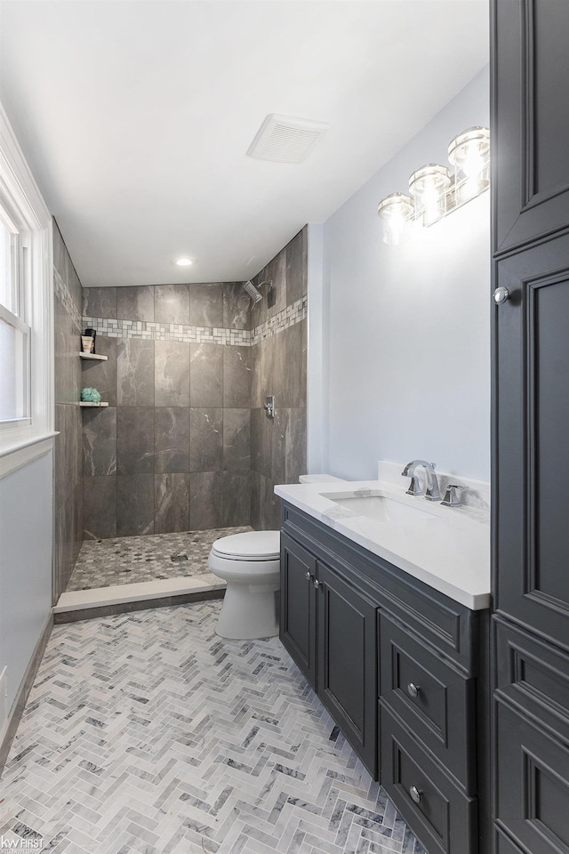 full bathroom with tiled shower, vanity, visible vents, and toilet