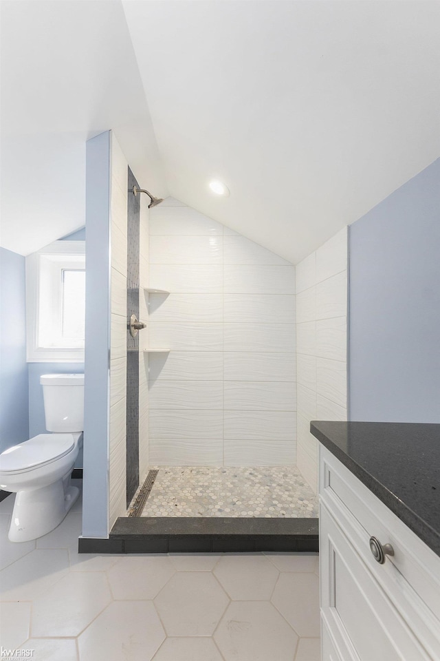 bathroom with a tile shower, toilet, tile patterned flooring, and vaulted ceiling