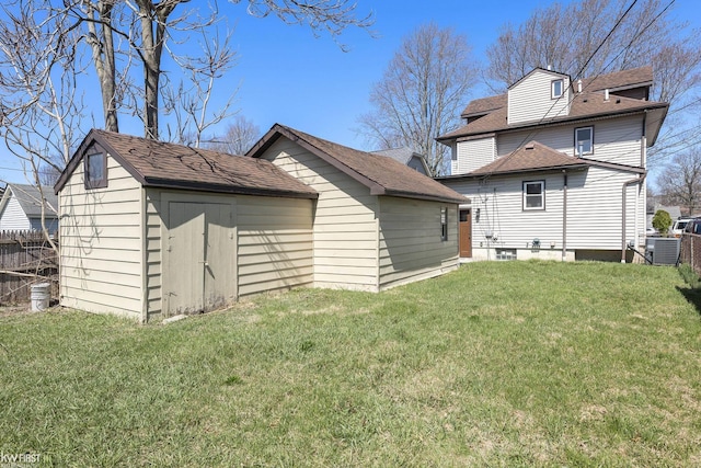 rear view of house with central AC, an outbuilding, a yard, fence, and a shingled roof