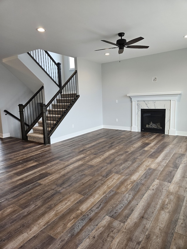 unfurnished living room with baseboards, ceiling fan, a fireplace, dark wood-style floors, and stairs