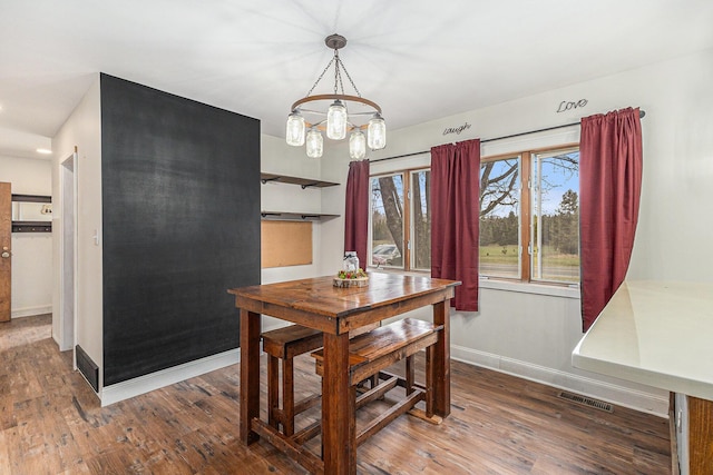 dining space with wood finished floors, baseboards, visible vents, and a notable chandelier