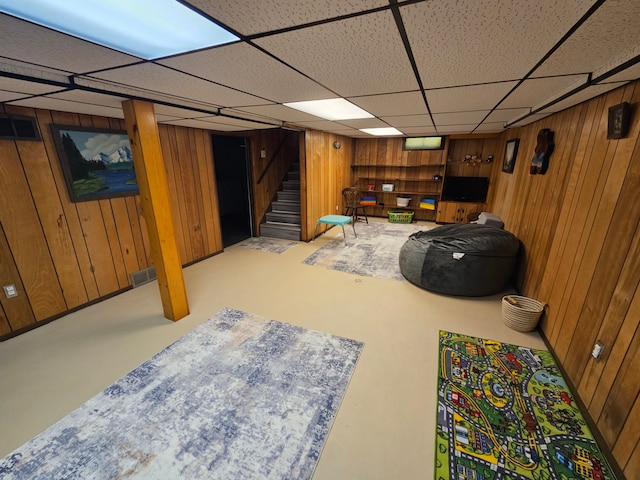 finished basement with stairs, wood walls, a drop ceiling, and visible vents