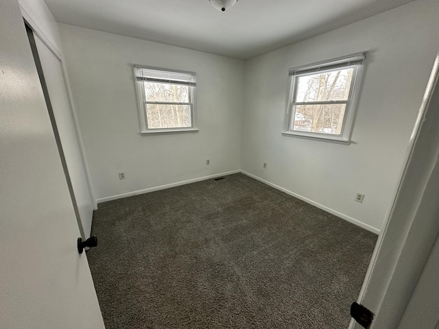 unfurnished bedroom featuring dark carpet, baseboards, and multiple windows