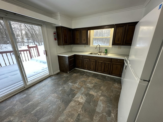 kitchen with stone finish floor, freestanding refrigerator, a sink, and dark brown cabinetry