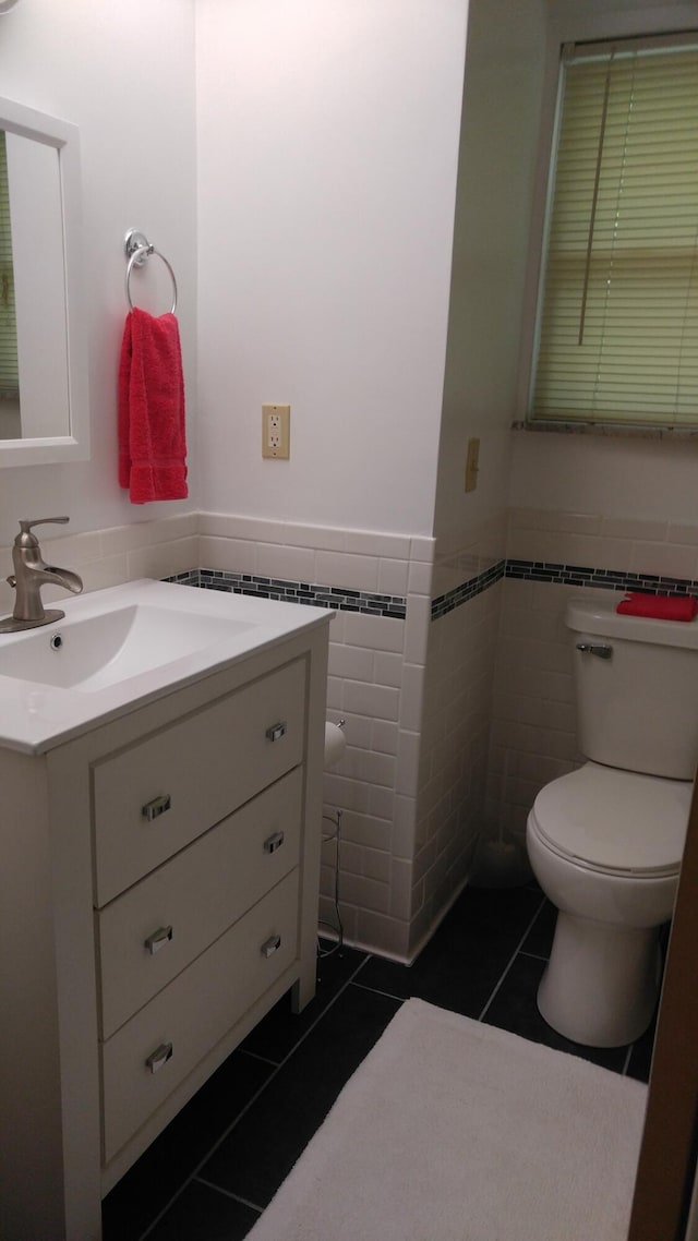 half bathroom with vanity, toilet, wainscoting, tile walls, and tile patterned floors