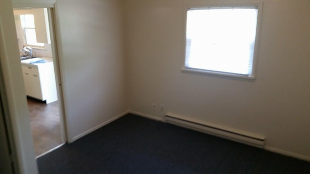 spare room with baseboards, a baseboard radiator, dark colored carpet, and plenty of natural light