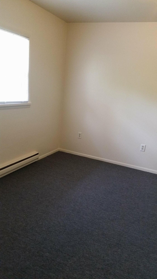 spare room featuring a baseboard radiator, dark colored carpet, and baseboards
