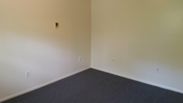 empty room featuring dark carpet and baseboards