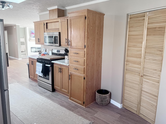 kitchen with ornamental molding, a textured ceiling, light countertops, light wood-style floors, and appliances with stainless steel finishes