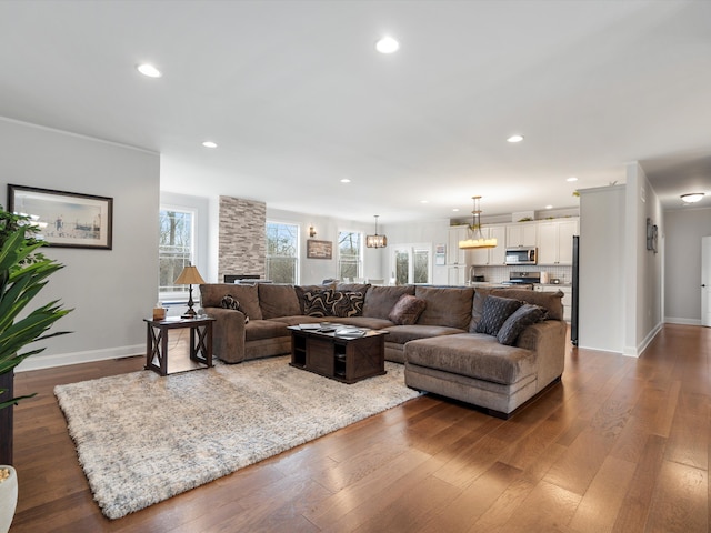 living area featuring recessed lighting, a stone fireplace, baseboards, and dark wood-style flooring