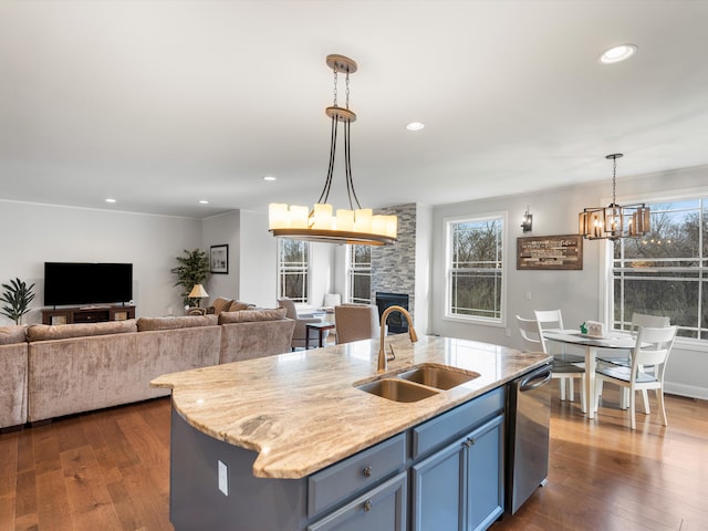 kitchen with a stone fireplace, stainless steel dishwasher, a sink, open floor plan, and a notable chandelier