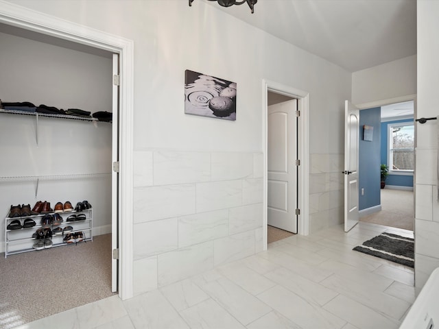 corridor featuring marble finish floor, tile walls, carpet flooring, and wainscoting