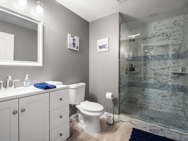 full bath featuring wood finished floors, toilet, vanity, a marble finish shower, and baseboards