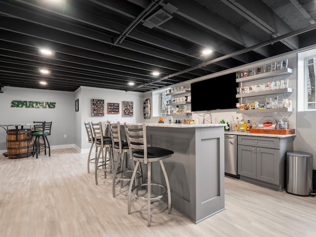 bar featuring light wood-type flooring, visible vents, baseboards, and indoor wet bar